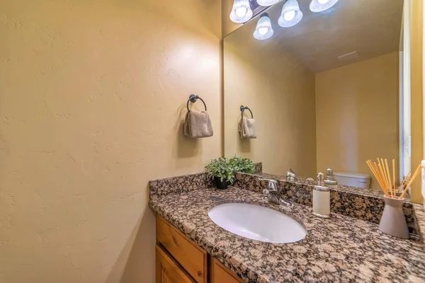 White oval sink on marble countertop with cabinet against huge mirror and light