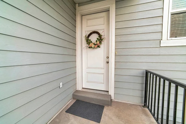 Puerta delantera blanca con corona floral contra revestimiento exterior de madera gris — Foto de Stock