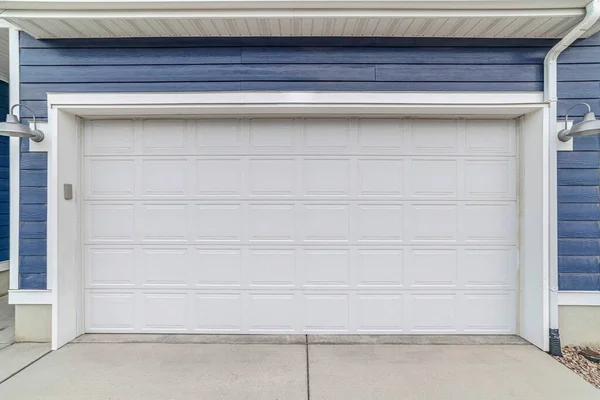 Wide white wooden garage door against blue exterior wall siding of house