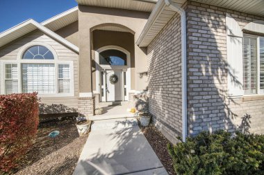 Evin dış tarafında çalılar, tuğlalar ve kemerli pencereler var.