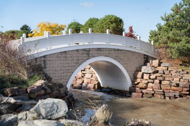 Beyaz parmaklıklı bir nehrin üzerindeki kemerli beton köprü.