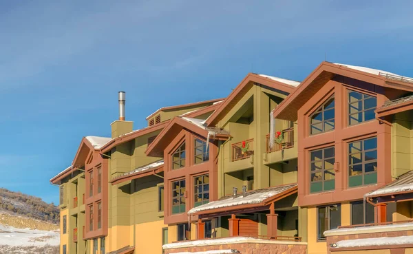 Casas con grandes ventanas de cristal y techos nevados contra colinas heladas y cielo azul — Foto de Stock