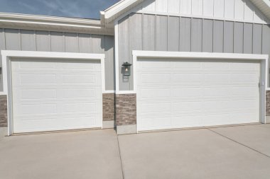 Kapalı çatılı ve gri duvarlı konut manzaralı iki araba garajı.