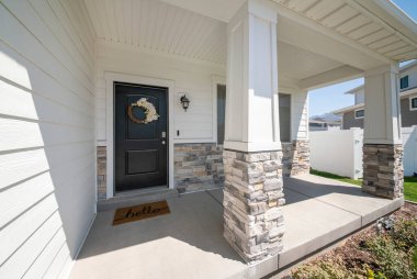 Siyah ahşap kapılı, çelenkli, beyaz duvarlı ve tuğlalı bir evin dışı.