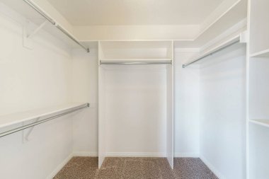 Boş bir dolabın içinde raflar, askılı çubuklar ve halı döşemeleri ile yürüyorum.