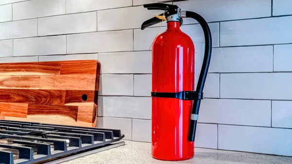 Alat pemadam api merah Pano terang terhadap kemiringan putih backsplash di dalam dapur rumah — Stok Foto
