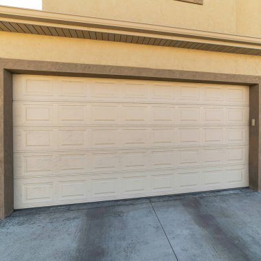 Duvarların arasında geniş beyaz panelli kapısı olan bir evin kare eklenmiş garajı.