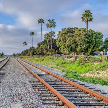 San Diego California 'da bulutlu mavi gökyüzüne karşı yol boyunca uzanan Square Railway rayları