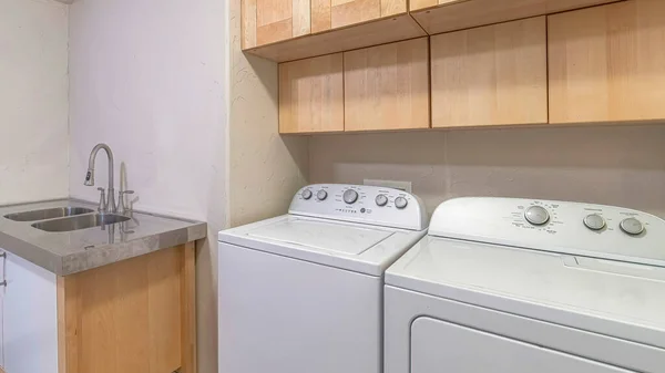 Pano Salle de lavage fonctionnelle avec appareils électroménagers et lavabo double vasque et armoires — Photo