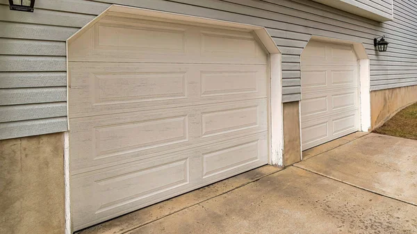 Pano, iki araba garajı ve gri duvar kaplamalı bir evin arka manzarası.