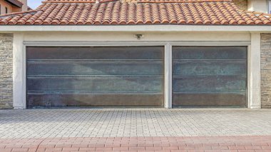 Garajında metal kapıları olan kırmızı kiremit çatılı ve tuğlalı garaj yolu olan Pano House.