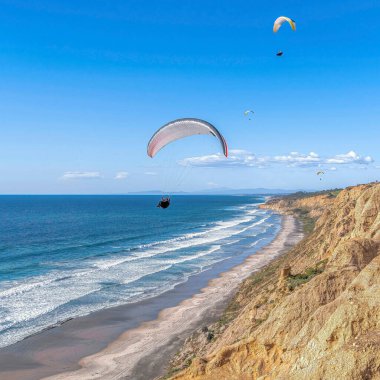 Kare Paraşütçüler San Diego California 'da mavi gökyüzüne karşı sahilin üzerinde uçuyorlar.