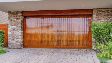Parlak kahverengi ahşap kapılı Pano House garajı taş tuğla duvar ve kapıya karşı.