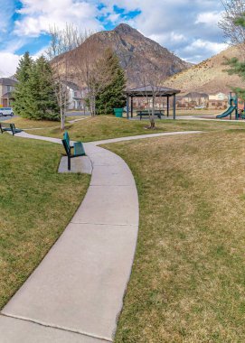 Dikey Dağ ve bulutlu gökyüzü çimlerin üzerinde patikaları ve ağaçları olan bir parka bakıyor.