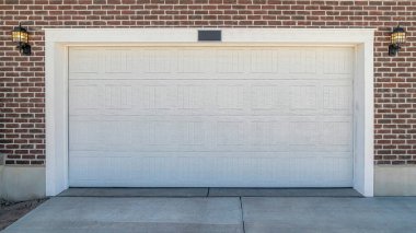 Pano, kırmızı tuğlalı dış duvara karşı geniş beyaz kapılı bir garaj inşa etti.