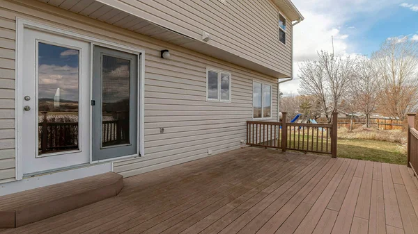 Pano Espaçoso deck de madeira de casa com vista para o quintal gramado com parque infantil — Fotografia de Stock