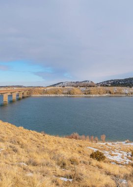 Dikey ve huzurlu bir göl. Kenarları kar, kenarları köprü.