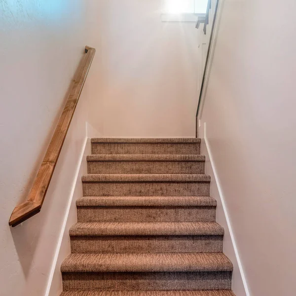 Square frame Stairway inside home with wall mounted wooden handrail and carpet on the treads