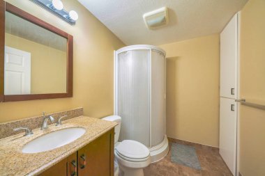 Banyo içi sarı duvarlarla ve yuvarlak duş muhafazasıyla dolu.