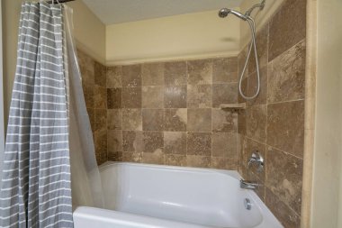 Küvetin içinde kahverengi fayanslarla çevrili bir banyo.