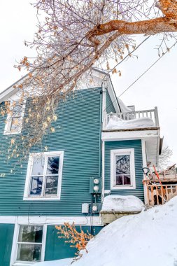 Üç katlı, karla kaplı mavi bir evin alçak açılı yan görüntüsü.