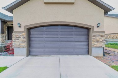 Yan tarafında iki tane lamba olan kemerli gri bir garaj kapısının dışı.