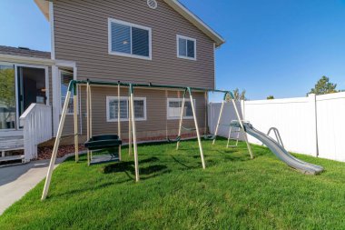 Beyaz vinil çitli bir evin arka bahçesinde oyun parkı.