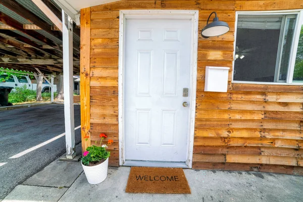 Porte d'entrée blanche décorée de fleurs sur un pot et paillasson avec panneau de bienvenue — Photo