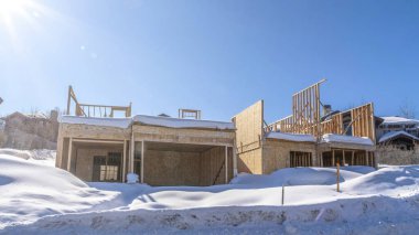 Park City Utah 'ta karlı bir mahallede Pano Home inşaat halinde. Tamamlanmamış evin üzerinde mavi gökyüzü ve parlak güneşli kış manzarası.