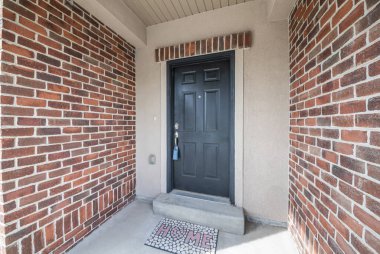 Duvarların ortasında tuğlalı kilit kutusu olan siyah ön kapı.