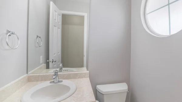 Pano banheiro branco pequeno com pia de cerâmica superior de mármore com armário azul e janela circular — Fotografia de Stock