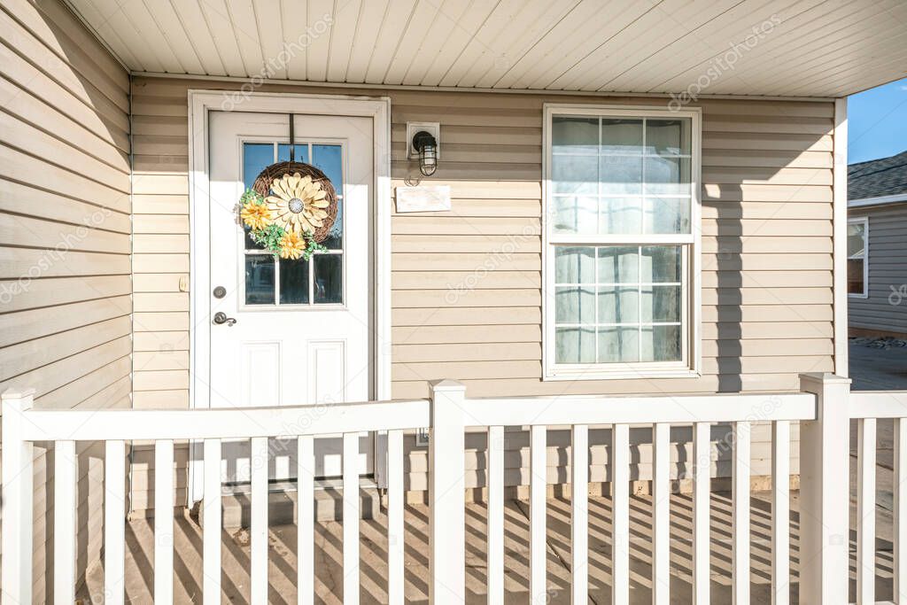 Porch of a house with beige vinyl wood siding and railing
