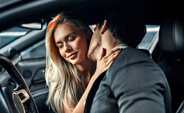 有激情的夫妻在车里做爱迷人的金发美女穿着典雅的黑色衣服 英俊的商人穿着西服 在车里接吻 — 图库照片
