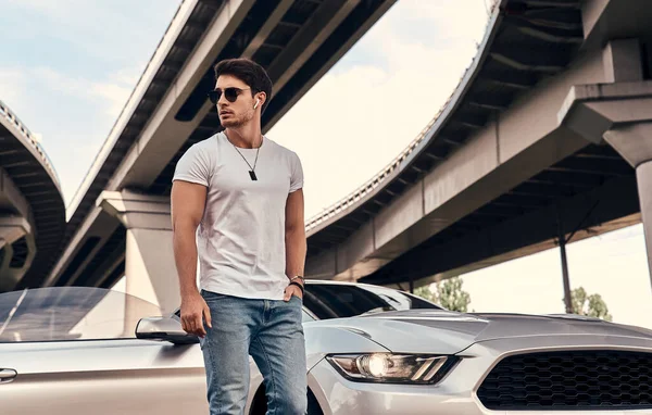 Handsome young man in casual clothes standing near his modern sport car on the street