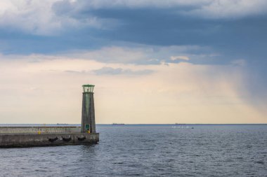 Kuzey Polonya 'da Baltık Denizi kıyısında. Kıyı feneri dramatik bir gökyüzüne karşı dik duruyor açık denizde gemilere ve denizcilere rehberlik ediyor. Huzurlu deniz manzarası.