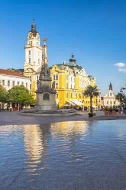 Pecs, Macaristan - 13 Temmuz 2024: Szechenyi Meydanı. Şehir meydanı tarihi binalar, merkezi bir anıt ve parlak mavi gökyüzünün altında su özelliği..