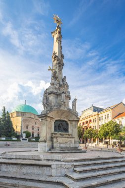 Pecs, Macaristan - 13 Temmuz 2024: Szechenyi Meydanı. Güneşli bir günde halka açık bir meydanda anıt ve bina. Arka planda bulutlu bulutlar olan açık gökyüzü..