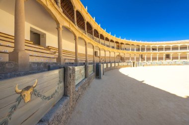 Ronda, İspanya - 4 Eylül 2024: The Plaza de Toros, Ronda 'da bir arenada. Açık mavi gökyüzünün altında boş bir boğa güreşi. Taş mimarisi ve ahşap koltuklar tarihi bir atmosfer yaratır..