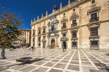 Granada, İspanya - 5 Eylül 2024: Granada Kraliyet Başbakanlığı. Güneşle ıslanmış bir kasaba meydanında tarihi bir bina. İnsanlar desenli meydanda yürür.