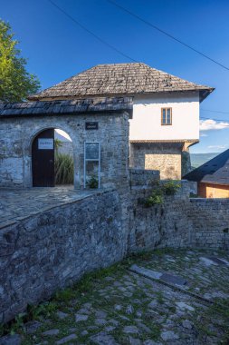 Jajce, Bosna-Hersek - 5 Temmuz 2024: Kemerli girişi, kiremitli çatısı ve açık mavi gökyüzü altında beyaz üst katı olan tarihi taş bina.