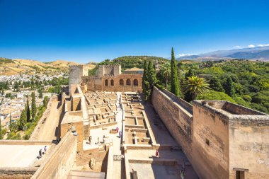 Granada, İspanya - 5 Eylül 2024: Alhambra kompleksindeki Alcazaba kalesi. Eski kalıntılar ve açık mavi gökyüzünün altındaki şehir manzarası. Tarihi ve nefes kesici manzaraları araştırın..