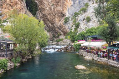 Blagaj, Bosna-Hersek - 9 Temmuz 2024: Blagaj Tekke manastırı yakınlarındaki Buna Nehri. Engebeli bir uçurumun kenarına kurulmuş bir restoran manzarası huzurlu bir yemek atmosferi yaratıyor..