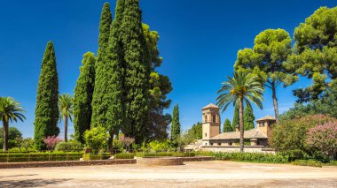Granada, İspanya - 5 Eylül 2024: Alhambra kompleksindeki Aziz Francis Manastırı. Yüksek ağaçlarla dolu sakin bir bahçe ve berrak mavi gökyüzünün altında tarihi bir bina..