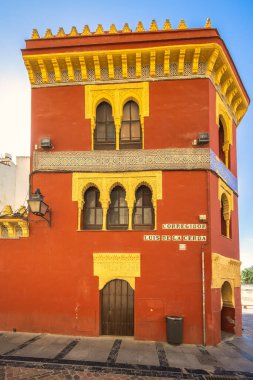Cordoba, İspanya - 7 Eylül 2024: Sarı aksanlı ve kemerli pencereli süslü kırmızı bina. Güneşli bir yerde geleneksel mimari.
