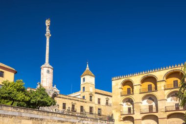 Cordoba, İspanya - 7 Eylül 2024: Canlı mavi gökyüzü altında tarihi mimari. Heykeli olan uzun bir kolon, eşsiz kemer ve detaylara sahip binaların yanında belirgin bir şekilde duruyor..