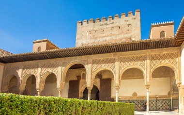 Granada, İspanya - 5 Eylül 2024: Alhambra Sarayı 'nın tarihi Nasrid Sarayı' ndaki Myrtles Sarayı 'nda doğu kemerleri. Süslü kemerler ve açık mavi gökyüzünün altında antik taş işçiliği.