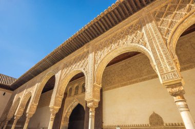 Granada, İspanya - 5 Eylül 2024: Alhambra Sarayı 'nın tarihi Nasrid Sarayı' ndaki Myrtles Sarayı 'nda doğu kemerleri. Mavi gökyüzünün altındaki tarihi bir binanın kemerleri ve süslü detayları..
