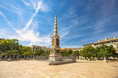 Malaga, İspanya - 12 Eylül 2024: Güneşli bir şehir meydanında, açık mavi gökyüzü altında ağaçlar ve binalarla çevrili bir anıt.