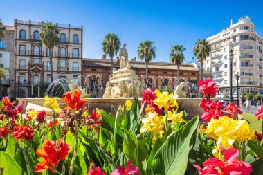 Seville, İspanya - 8 Eylül 2024: Canlı çiçekler tam çiçek çerçevesi üzerinde güneşli bir gökyüzü altında bir çeşme ve mimari.