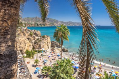 Nerja, İspanya - 9 Eylül 2024: Europa Meydanı 'ndan görüntü. Palmiye yaprakları, turkuaz su ve kayalık kayalıklarla çerçevelenmiş güneşli plaj.